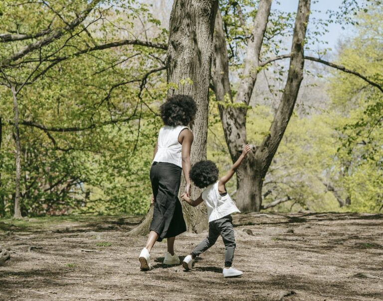 A mother and son walk hand-in-hand through a lush, sunny forest in spring.