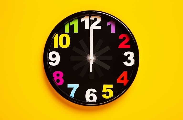 Vibrant wall clock with colorful numbers on a bright yellow background, emphasizing modern decor.